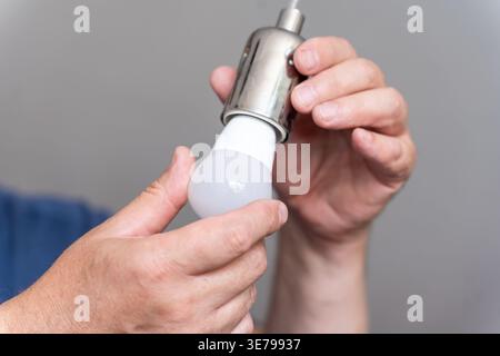 A Caucasian hand replaces an LED lamp in a minimalist interior, highlighting routine, energy awareness, and focus. The tactile detail of LED setup exp Stock Photo