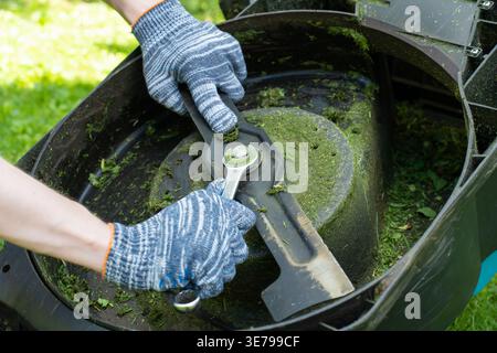 A close-up of gloved hands adjusting the blade of a flipped lawn mower, symbolizing self-reliance and hands-on maintenance. Stock Photo