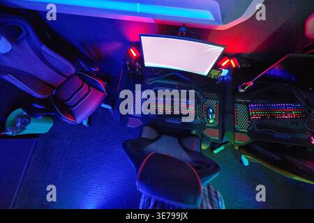 Top Down View of RGB Gaming Setup With Dual Keyboards, Curved Monitor and Racing Chairs in Neon Light Stock Photo
