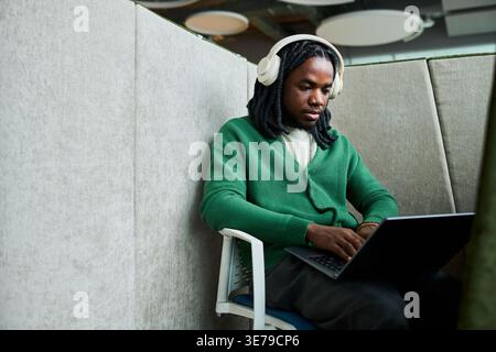 Black Man Using Laptop and Headphones for Focused Office Work Stock Photo