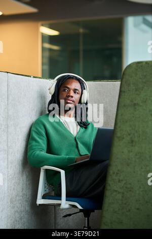 Black Man Wearing Headphones Working on Laptop in Office Booth Stock Photo
