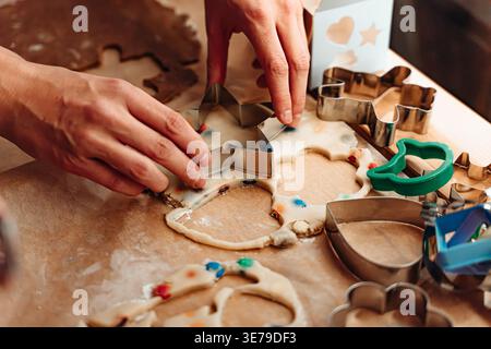 Hands press metal star cutter into rolled cookie dough decorated with colorful candies, cozy family Christmas tradition Stock Photo