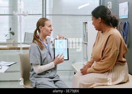 Female Doctor Showing IVF Process on Tablet to Black Woman Patient Stock Photo