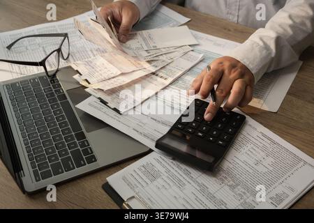 Hands using calculator with receipts and financial documents while performing expense calculation and budget planning process for accounting, financia Stock Photo