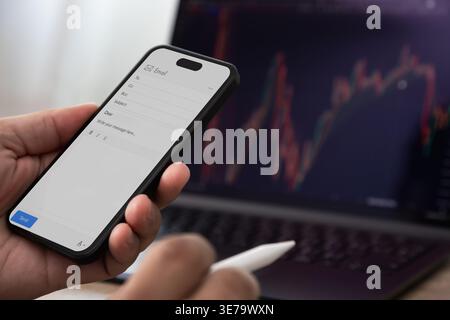 Smartphone displaying email compose screen with stylus near laptop showing chart, enabling mobile message communication workflow for business correspo Stock Photo