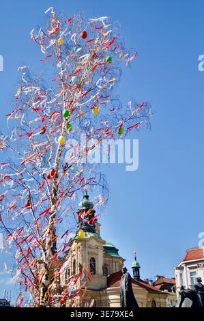 Colorful Easter tree decorated with ribbons and painted eggs stands in a historic city square beside baroque church towers, creating a festive spring Stock Photo