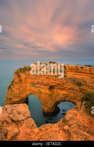 A serene sunrise photograph captured from the cliffs of Praia da Marinha in the Algarve, featuring the famous natural rock formation known as the “Hea Stock Photo