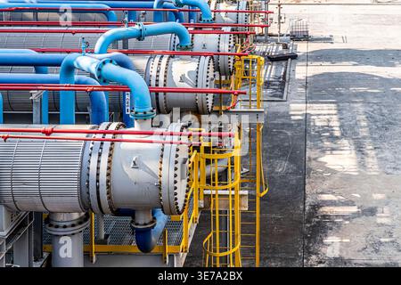 Industrial scene featuring large metallic pipes and cylindrical tanks. Blue and red pipes run horizontally across frame. Yellow safety railings line e Stock Photo