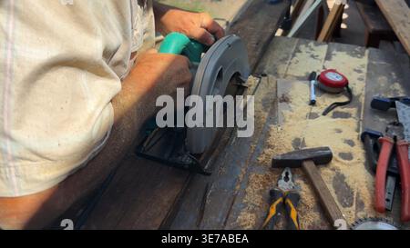 Arms of professional repairman sawing wooden construction with a circular saw at construction. Male hands of adult craftsman cuts wood using electric Stock Photo