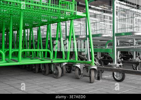 Rows of green and chrome shopping carts in a store parking lot. Modern metal shopping trolleys stacked together near a supermarket entrance. Stock Photo