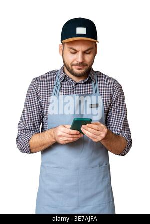 Front view of isolated male entrepreneur in apron and cap using smartphone. Stock Photo
