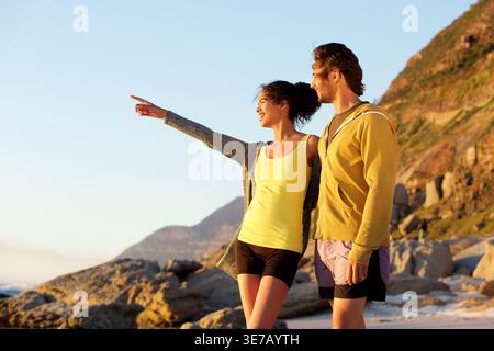 Smiling Black woman pointing away standing and looking away with caucasian boyfriend outdoors on sunny day Stock Photo