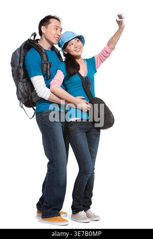 Smiling Chinese couple taking picture using camera standing closed together against white background in studio Stock Photo