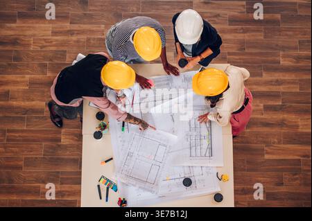 Overview Diverse group of engineers  wearing safety helmets working on blueprints on the table inside the office Stock Photo