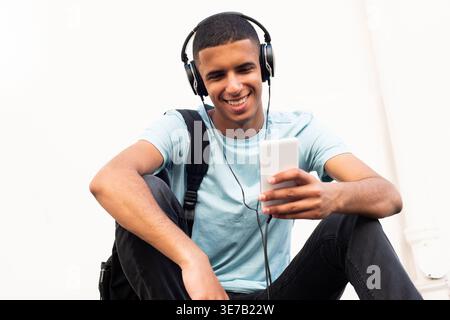 Arab male using cellphone leaning arms on knees sitting on ground against white wall Stock Photo
