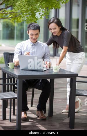 Chinese male and female office workmates working together on laptop in outdoor cafe Stock Photo