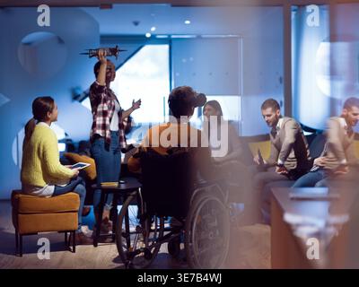 Diverse group of business people with disabled caucasian businessman using VR goggles and drone assistance simulation while having a meeting in the... Stock Photo