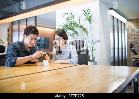 Smiling Chinese IT workers holding and looking at clear glass working together developing smartphone in office Stock Photo