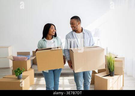 Smiling Black couple looking at each other holding cardboard boxes while standing in living room at home Stock Photo