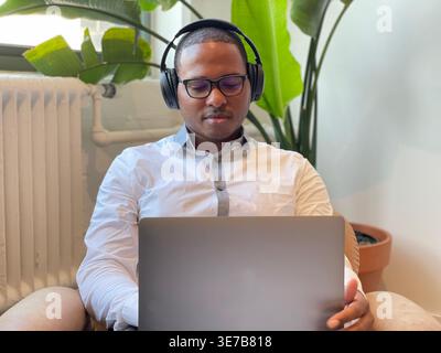 Black man wearing headphones using laptop while sitting on couch in office Stock Photo