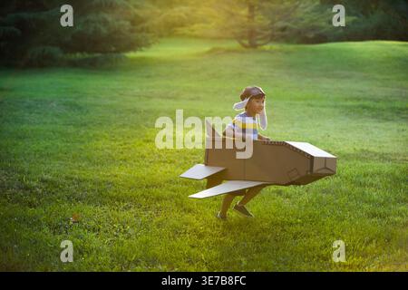 Cheerful Chinese boy in airplane cardboard box costume playing in park at sunset Stock Photo