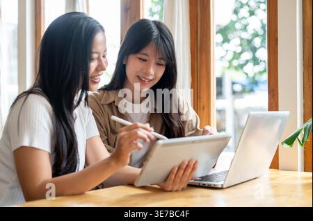 Asian female friends discussing over tablet while sitting together in cafe Stock Photo