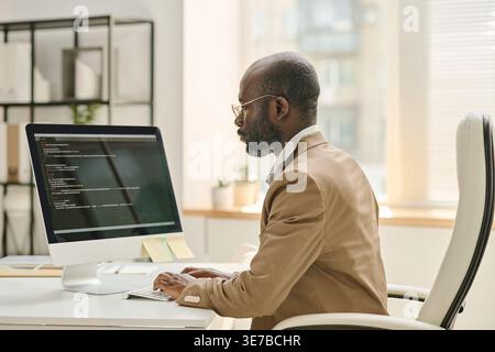 Black male programmer wearing eyeglasses working on computer while sitting at desk in office Stock Photo