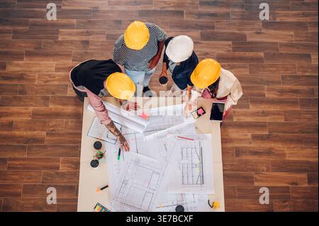 Overview Diverse group of engineers  wearing safety helmets working on blueprints on the table inside the office Stock Photo