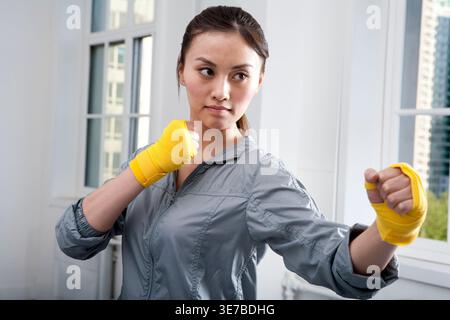 Determined Chinese woman with hand wrap throwing punches during training in gym Stock Photo