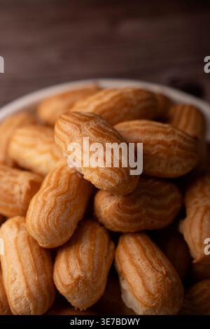 close-up of a pile of golden-brown mini éclairs (choux pastries) in a bowl on a wooden tabletop, warm tones and crisp ridged texture with visible crea Stock Photo