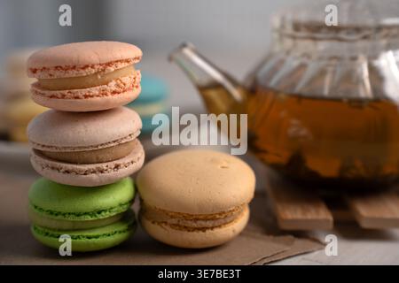 close-up of pastel macarons stacked beside a glass teapot of amber tea on a wooden tabletop, soft natural light creating a cozy, delicate, intimate mo Stock Photo