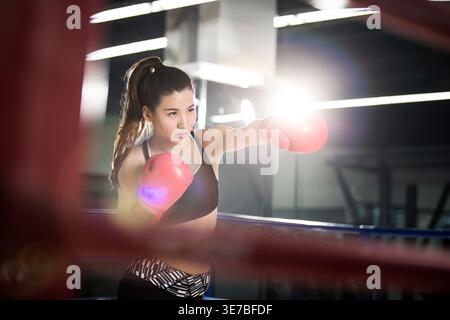 Serious Chinese female boxer wearing boxing gloves throwing punches while practicing in boxing ring Stock Photo