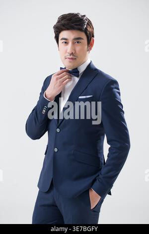 Mixed race man in formal suit adjusting bow tie while standing with hand in pocket against white background in studio Stock Photo