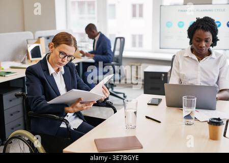 Serious Black businesswoman using laptop working with caucasian colleagues sitting at table in office Stock Photo