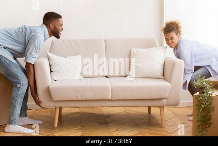 Tired Black couple lifting and moving sofa together after moving in new home Stock Photo