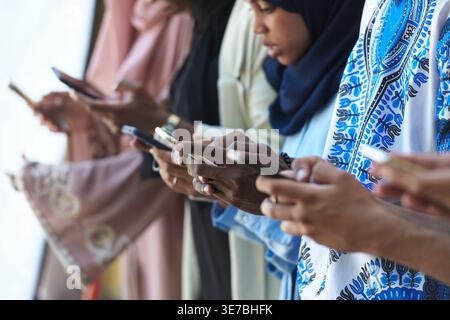 Diverse group of friends using their smartphones while standing together and leaning against yellow wall Stock Photo