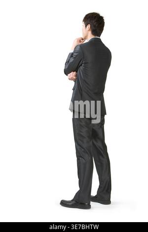 Chinese businessman touching chin standing facing white background in studio Stock Photo