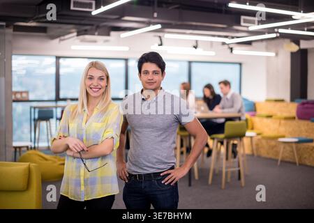 Mixed race businessman and caucasian business woman standing together near colleagues having a meeting in the office Stock Photo