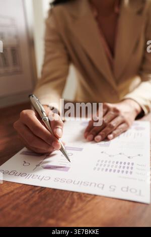 Female designer making corrections in infographics while standing at table in office Stock Photo