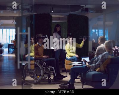 Diverse group of business people with disabled caucasian businessman using VR goggles and drone assistance simulation while having a meeting in the... Stock Photo