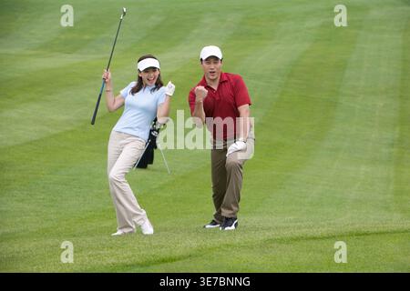 Smiling Chinese couple playing golf while standing on golf course Stock Photo
