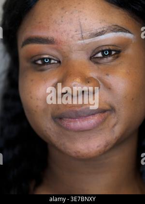 Black female client with white dye on her eyebrows waiting for threading while sitting in salon Stock Photo