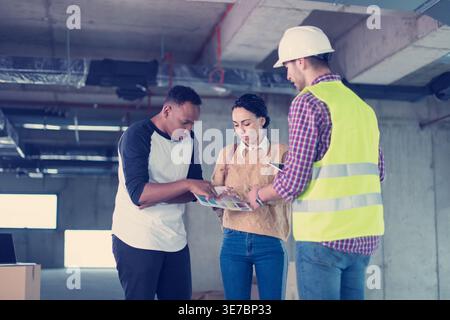 Middle Eastern woman and Black man standing and talking to caucasian male architect explaining plans inside the building Stock Photo