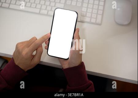 Man wearing maroon hoodie using smartphone while sitting at table in office Stock Photo