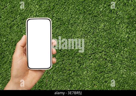 Hand holding smartphone with blank screen on green grass background mockup Stock Photo