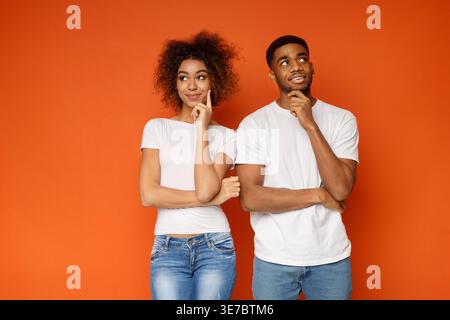 Black couple touching cheek and thinking looking away while standing against orange background in studio Stock Photo