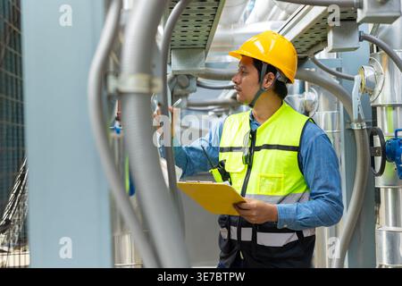 Asian male engineer wearing safety helmet holding clipboard checking pipeline standing on rooftop during daytime Stock Photo