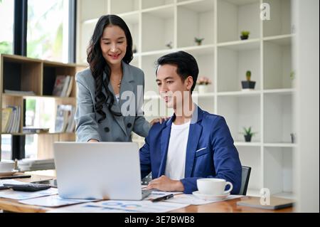 Smiling Asian business woman training and briefing a male worker in the office on a new project Stock Photo