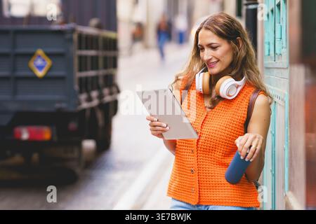 Colombian woman holding water bottle using tablet standing on city street during daytime Stock Photo