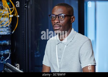 Black male IT engineer with eyeglasses standing in server room in data center Stock Photo